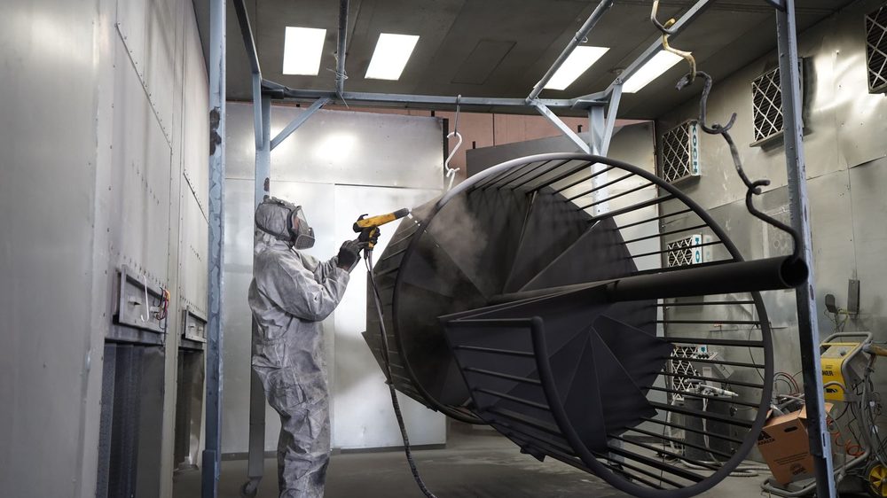 Powder coating a metal part in a spray booth (illustrative stock photo)